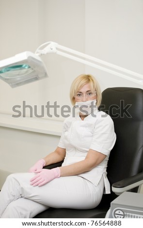 Nurse in respiratory bandage is sitting on pedicure chair and looking at you