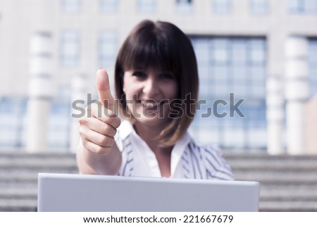 Business woman sitting on the stairs gives thumbs up for business success