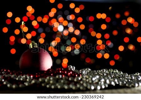 Red Christmas bauble on red and silver pearls with red bokeh background in dark