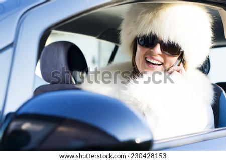 Beautiful woman in white fur coat speaking on the phone in car
