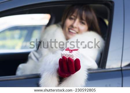 Woman holding a white gift box with red dots wearing red gloves in car