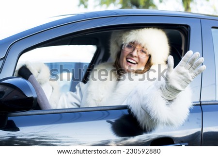 Beautiful woman in white fur coat waving from an open car window