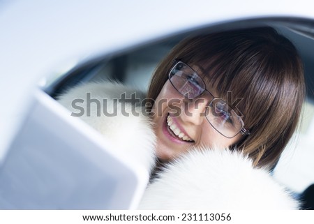 Beautiful woman in white fur coat smiling while using computer in a car