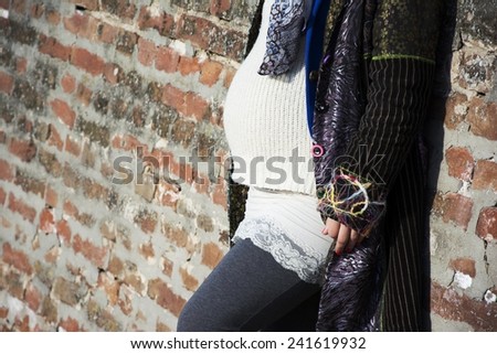 Pregnant woman standing leaned on a brick wall