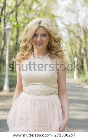 Beautiful blond curly woman wearing evening peach color gown running and looking aside. Fashionable and glamorous dress and style.