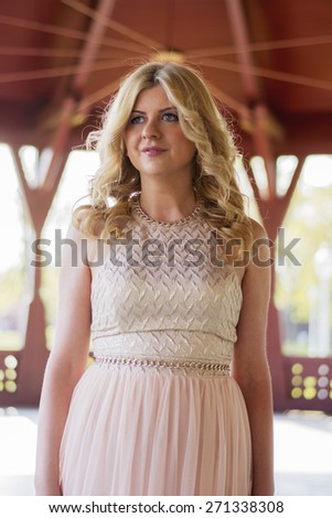Portrait of beautiful blond curly woman wearing evening peach color gown in outdoors. Fashionable and glamorous dress and style.