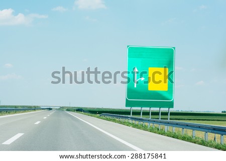 Board on the right side of high way with yellow and green space for directions