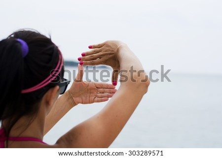 Woman making viewfinder shape out of her hands looking towards the sea