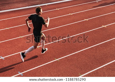 Image of handsome strong young sportsman running outdoors.