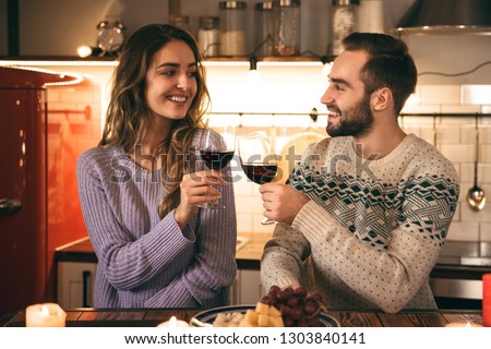 Beautiful happy young couple spending romantic evening together at home, drinking red wine, toasting
