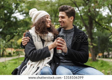 Portrait closeup of smiling people man and woman 20s hugging and holding thermos cup while walking resting in green park