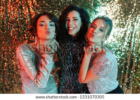 Three cheerful beautiful women wearing bright clothes having a party over sparkling background