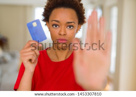 Young african american woman holding credit card with open hand doing stop sign with serious and confident expression, defense gesture
