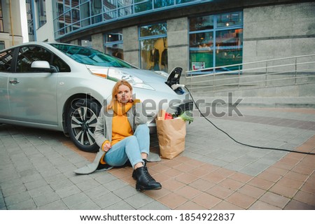Charging electro car at the electric gas station. Woman by the car.