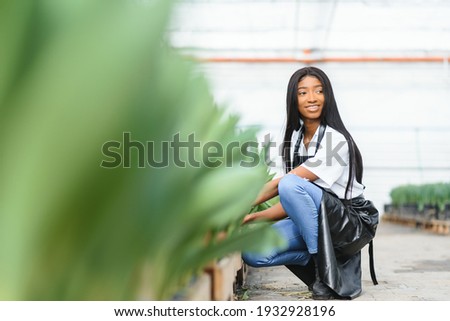 Beautiful young smiling african american girl, worker with flowers in greenhouse. Concept work in the greenhouse, flowers.