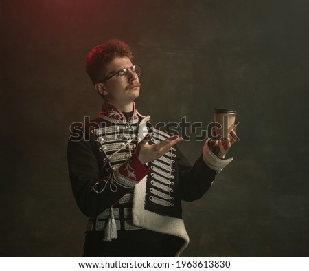 Coffee break. Young man in suit as royal person isolated on dark green background. Retro style, comparison of eras concept. Beautiful male model like historical character, monarch, old-fashioned.