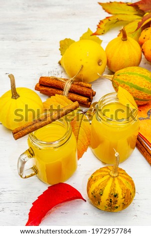 Non-alcoholic spicy orange cocktail. Festive Halloween drink, decorative pumpkins, fall leaves and cinnamon sticks. White wooden boards background, close up