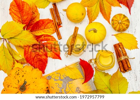 Non-alcoholic spicy orange cocktail. Festive Halloween drink, decorative pumpkins, fall leaves and cinnamon sticks. White wooden boards background, top view
