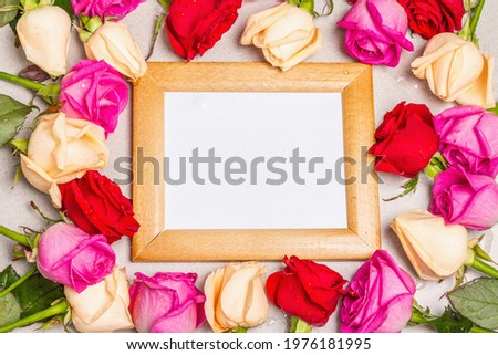 Multicolored fresh roses and a wooden frame on light stone background. Festive gift, greeting card for Easter, Birthday, Valentines Day or Wedding. Holiday concept, a place for text