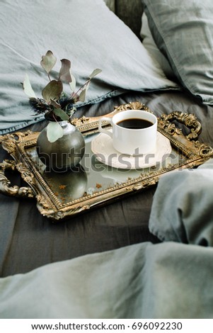 Morning coffee on golden vintage tray in bed with grey sheet and pillows.