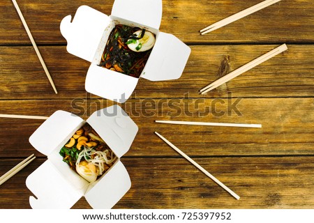 Noodles in box and chopsticks on wooden table background. Flat lay, top view. Chinese takeaway food concept.