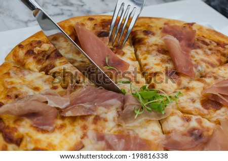 Cutting a delicious pizza with fork and knife on plate