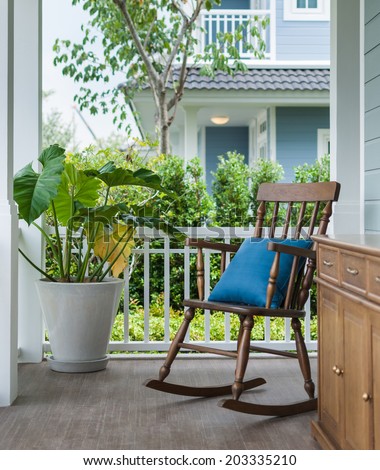 wooden rocking chair on front porch with pillow and planter
