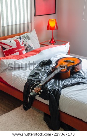 modern bedroom with guitar and jacket on white bed at home