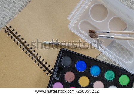 Set of watercolor paints, brushes for painting and blank paper sheet of sketchbook