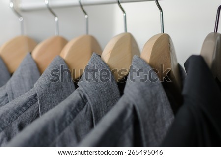 close up row of grey and black shirts hanging on coat hanger in white wardrobe