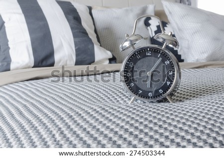 modern alarm clock on black and white bed at home