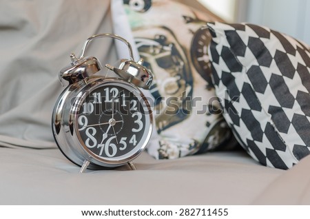 modern alarm clock on black and white bed at home