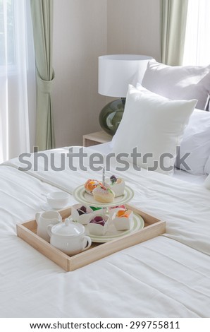 wooden ray of tea set and cup cake on white bed in modern bedroom