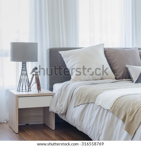 pillows on modern bed with grey lamp on wooden table side in modern bedroom