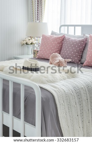 pink pillows with pink doll on white wooden bed and classic hat in bedroom
