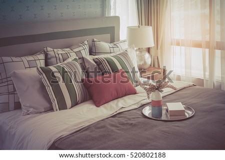 colorful pillows on white bed in modern bedroom design with tray of book and plant, vintage process style