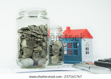 Coins, jar and house in the background isolated on white