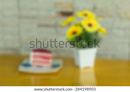 Strawberry layer cake on white dish and   yellow artificial flowers in a white vase rests on yellow wooden table blurred background