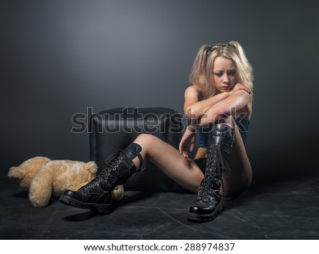 Beautiful teenager with blond hair in the style of anime in black army boots sitting on the dirty floor