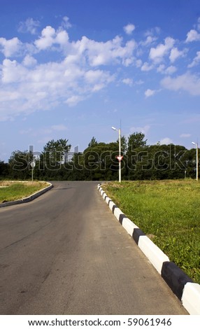 Road sign on the crossroads. Landscape with a rural road, bright sky and grass on the side.