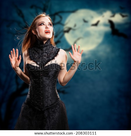 attractive vampire in front of a dark landscape with full moon and flying bats