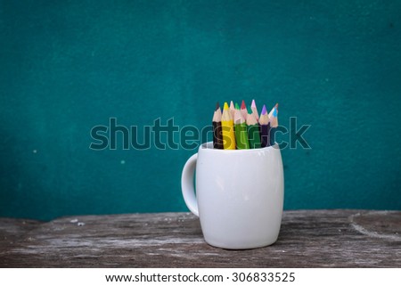color pencil in a white cup on wood texture