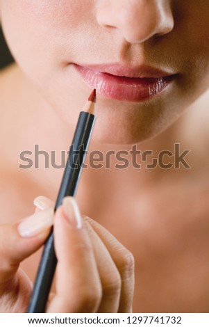 Studio beauty shot with young woman using lip pencil against black