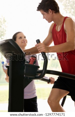 Young man exercising on cross trainer with female personal trainer
