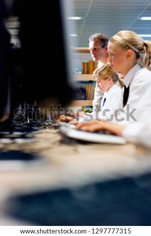 Line of high school students in uniform using computers in library