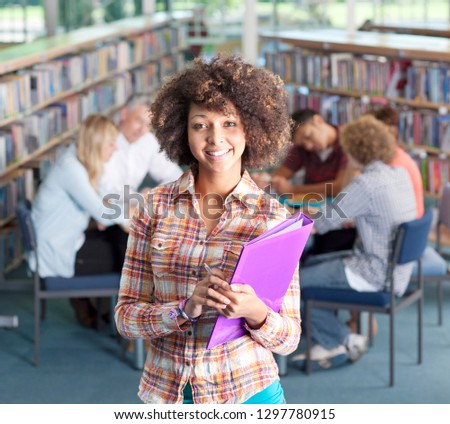 Female high school student in library holding folder smiling at camera