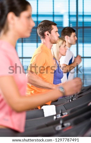 Active men and women exercising on running machines in gym