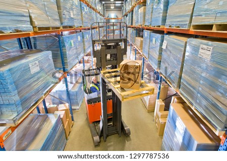 Distribution warehouse worker moving cardboard box on forklift truck