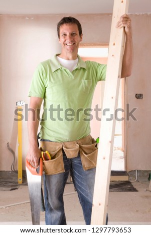 Smiling male carpenter holding timber plank at camera
