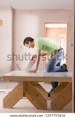 Carpenter with saw cutting timber inside house on construction site